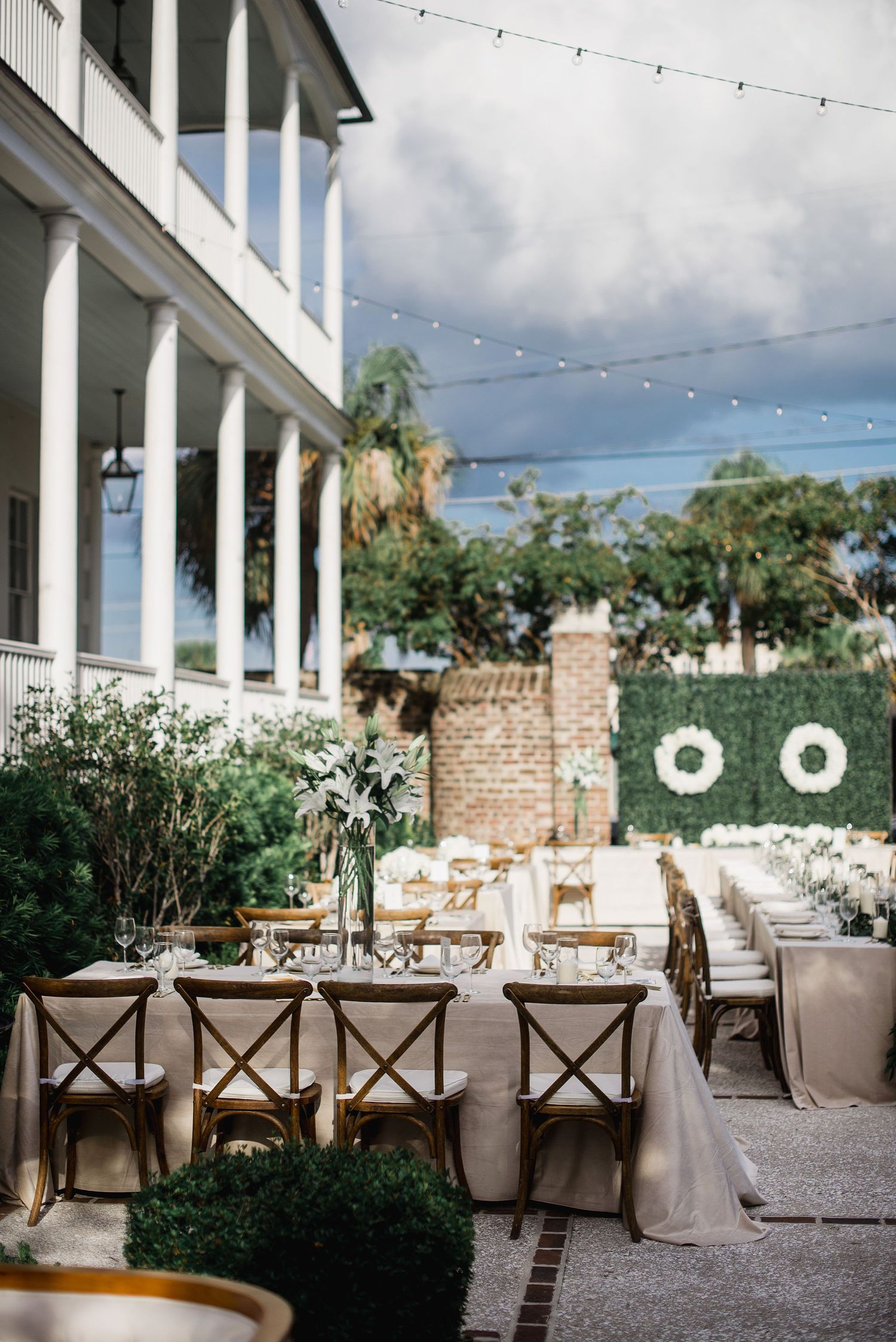 Elegant outdoor wedding reception venue with white columns, string lights, and rustic wooden chairs at dining tables.