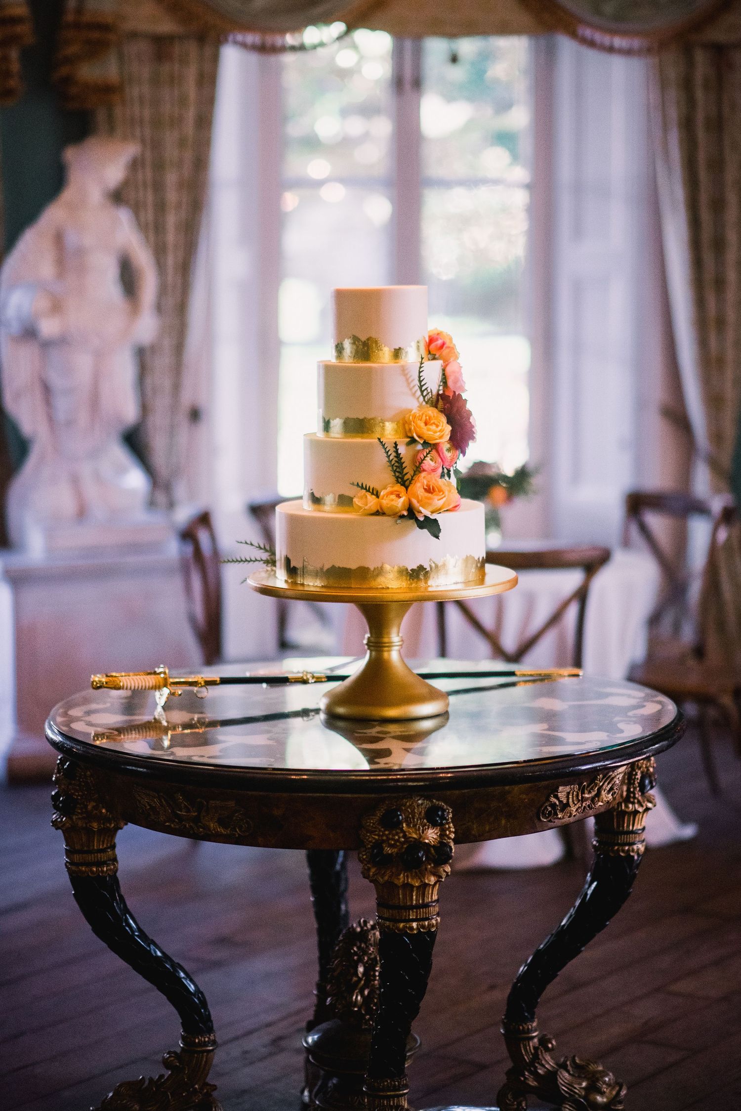 Three elegant wedding cakes displayed on ornate black antique tables with gold accents and floral decorations.