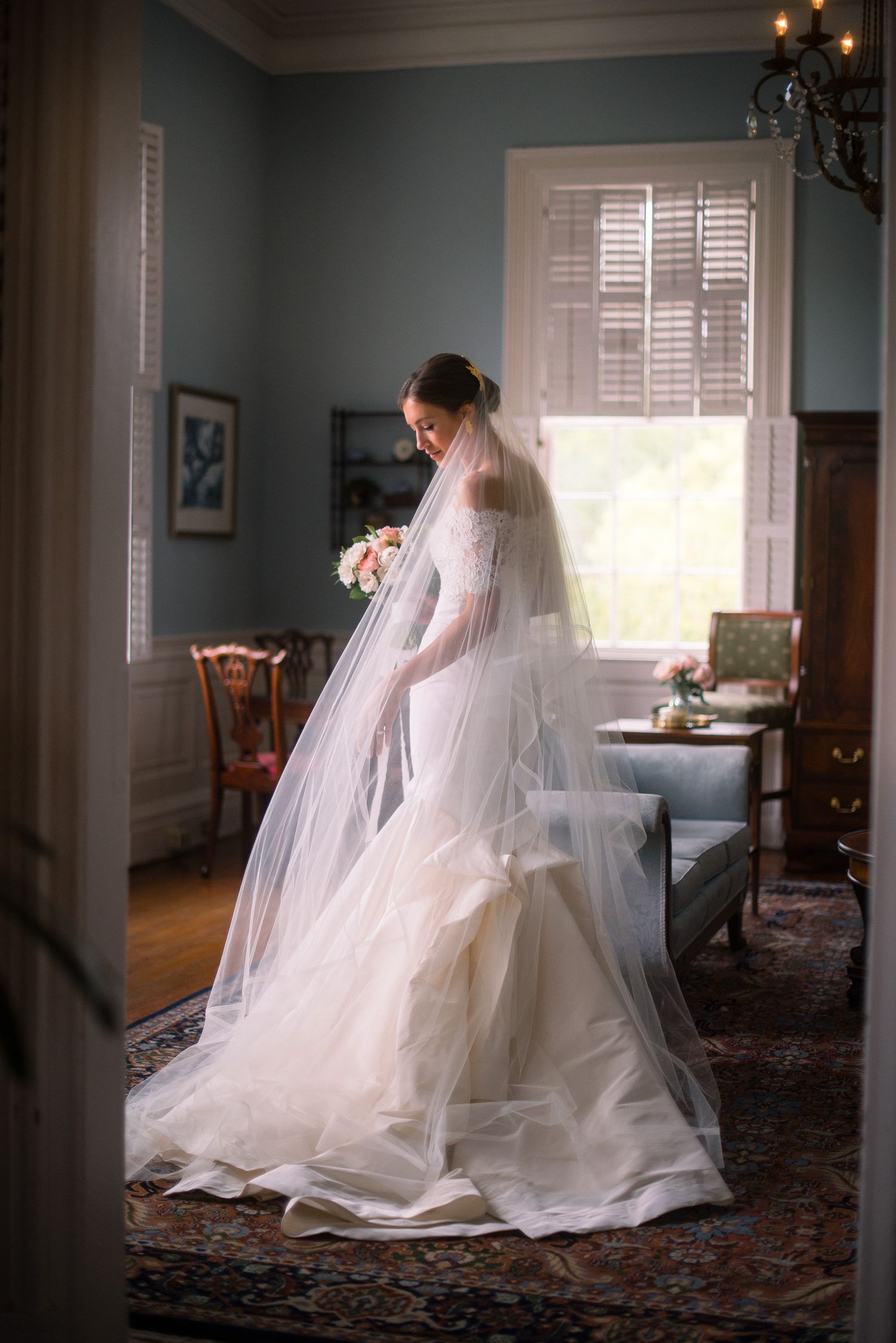 A flowing white wedding dress and veil create an ethereal silhouette against a softly lit interior room.