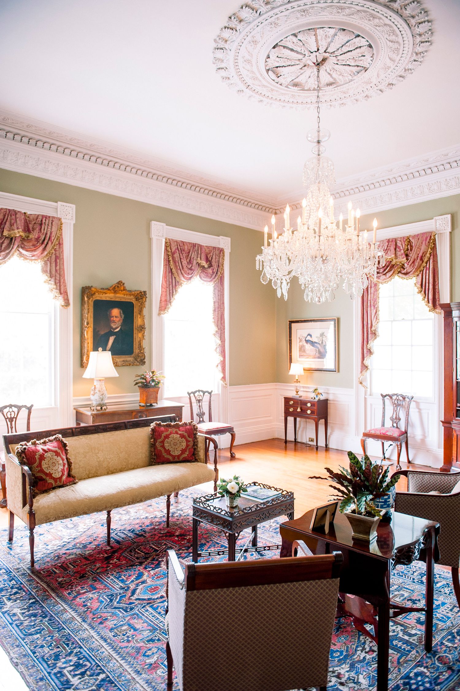 Elegant Victorian parlor room with ornate ceiling medallion, crystal chandeliers, period furniture and blue oriental rugs.