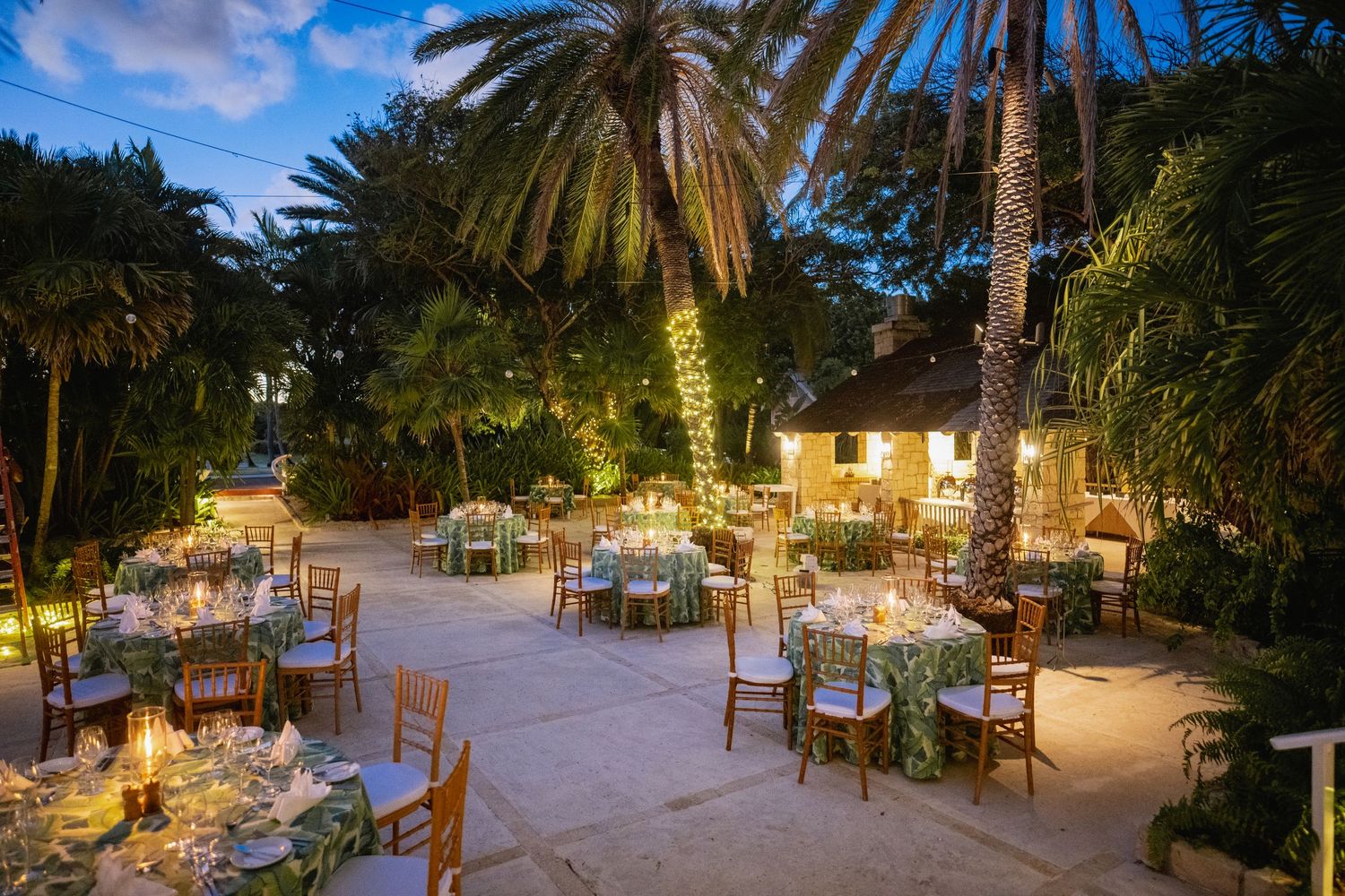 Tropical wedding venue at dusk with palm trees and outdoor dining setup.