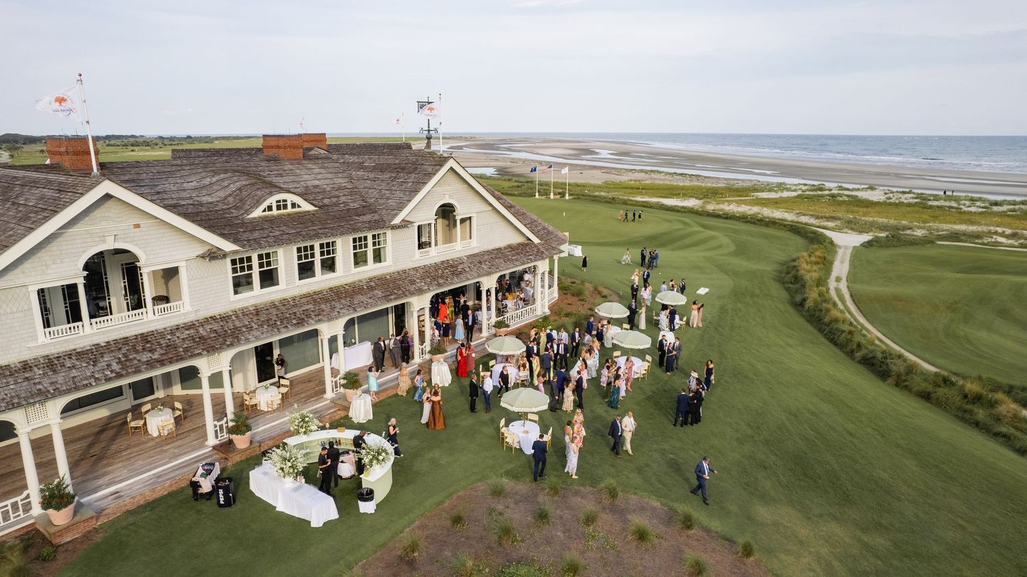 Aerial view of a wedding reception gathering at a coastal golf club with ocean views and elegant clubhouse.