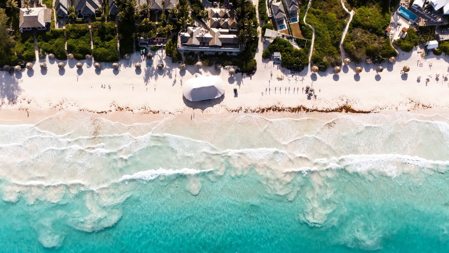 Aerial view of pristine turquoise waters meeting white sandy beaches along a tropical coastline.
