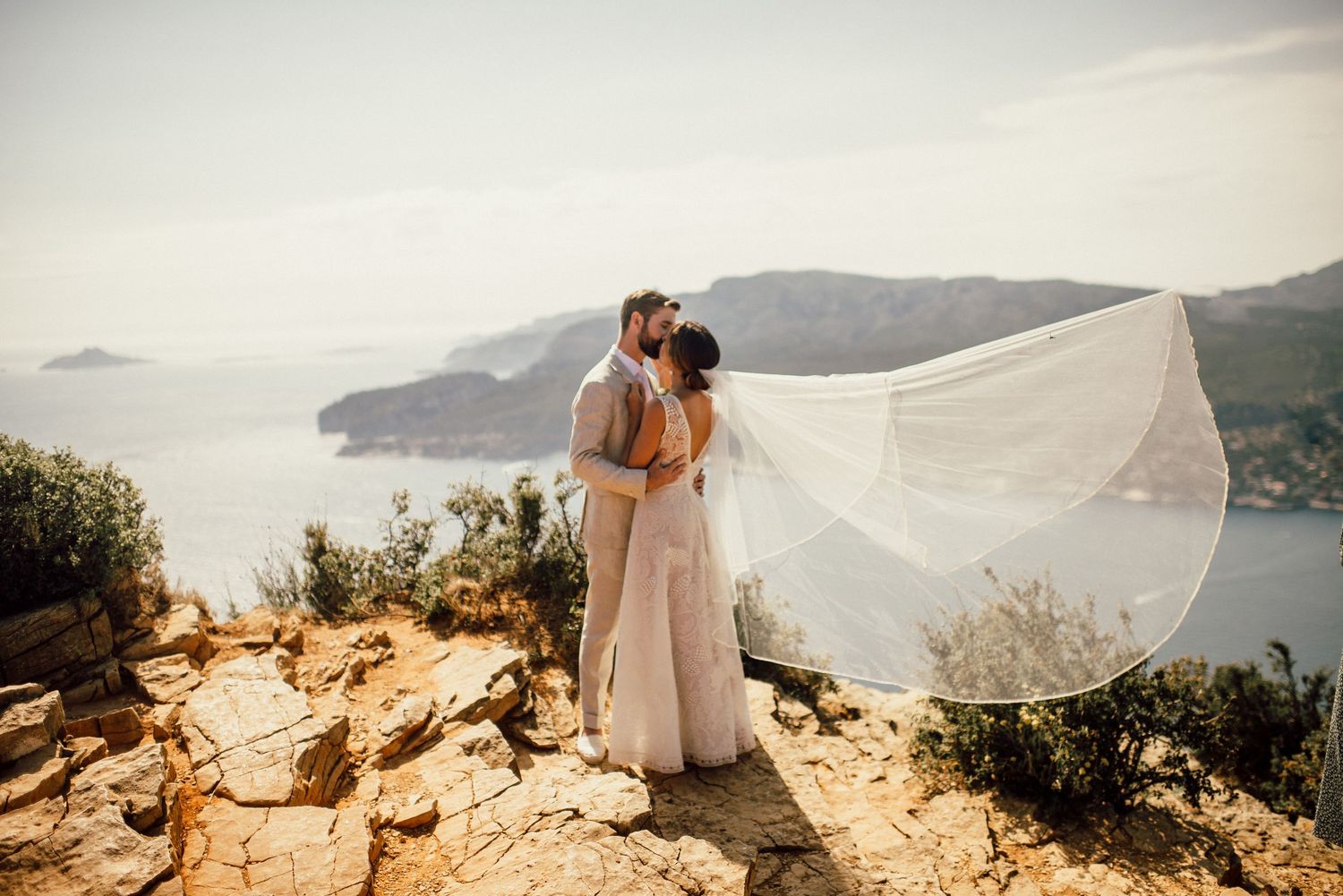 A romantic couple embraces on a scenic coastal cliff overlooking the Mediterranean Sea during golden hour.