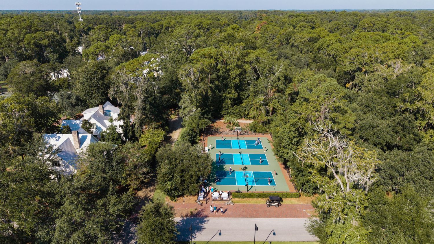 Aerial panoramic view of a resort pool and tennis courts surrounded by lush forest canopy.