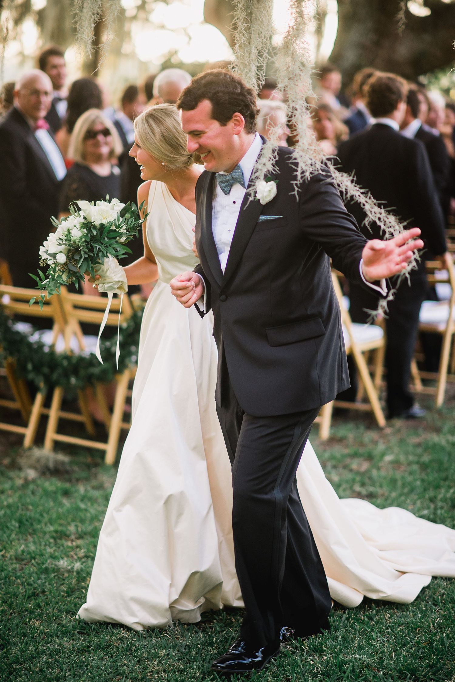 Newlyweds share their first dance on a lawn during an outdoor wedding ceremony with guests looking on.