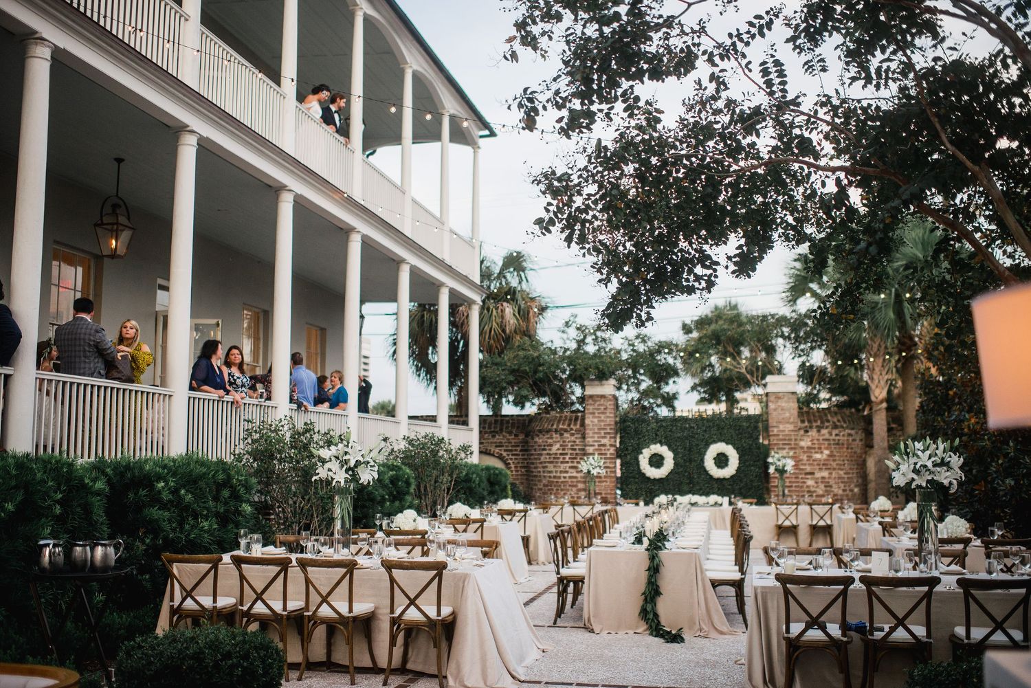 Wedding reception setup at a classic Southern plantation house with white columns and outdoor dining tables at dusk.