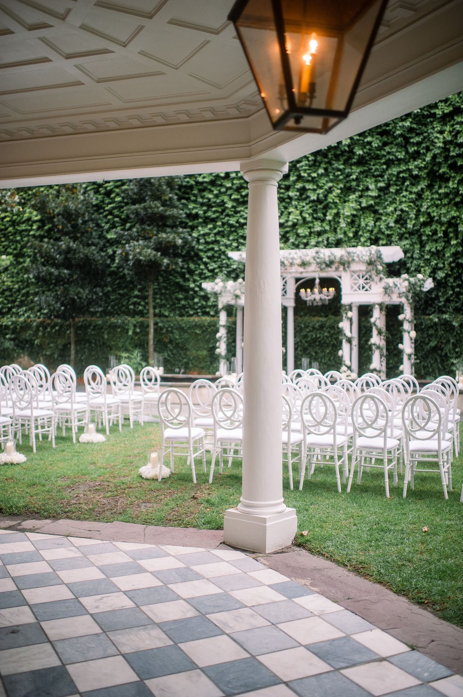 White chairs arranged in rows under a covered outdoor patio with columns and ivy-covered walls for a wedding ceremony.