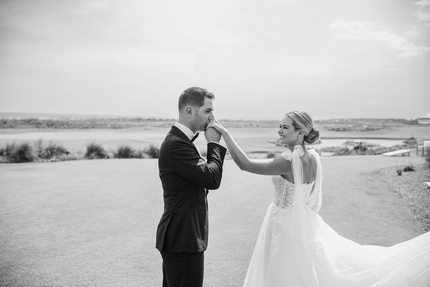 A couple in formal wedding attire embraces on a beach during sunset, creating a romantic silhouette against the horizon.