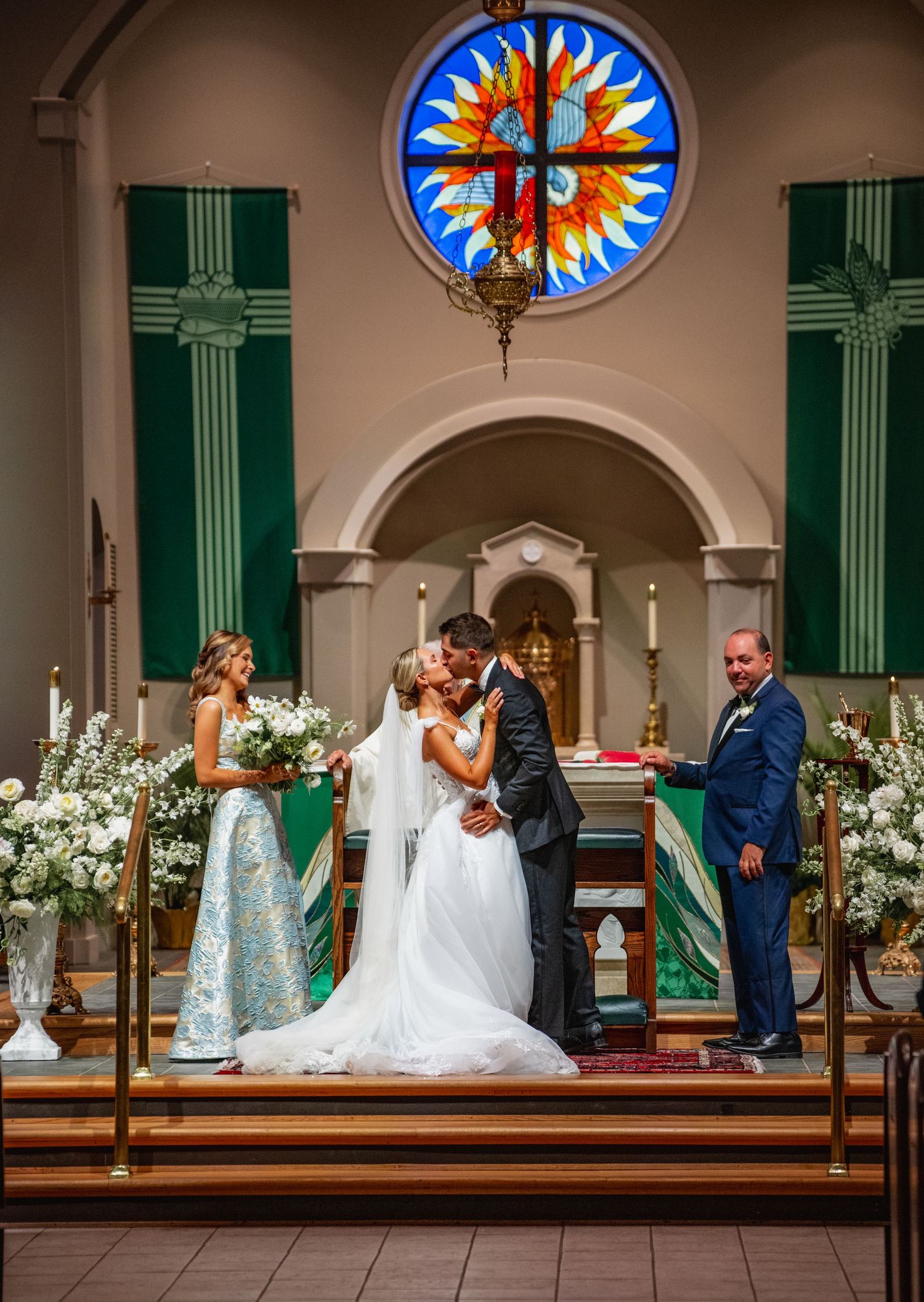 Church ceremony with stained glass windows and white floral arrangements decorating the altar area.