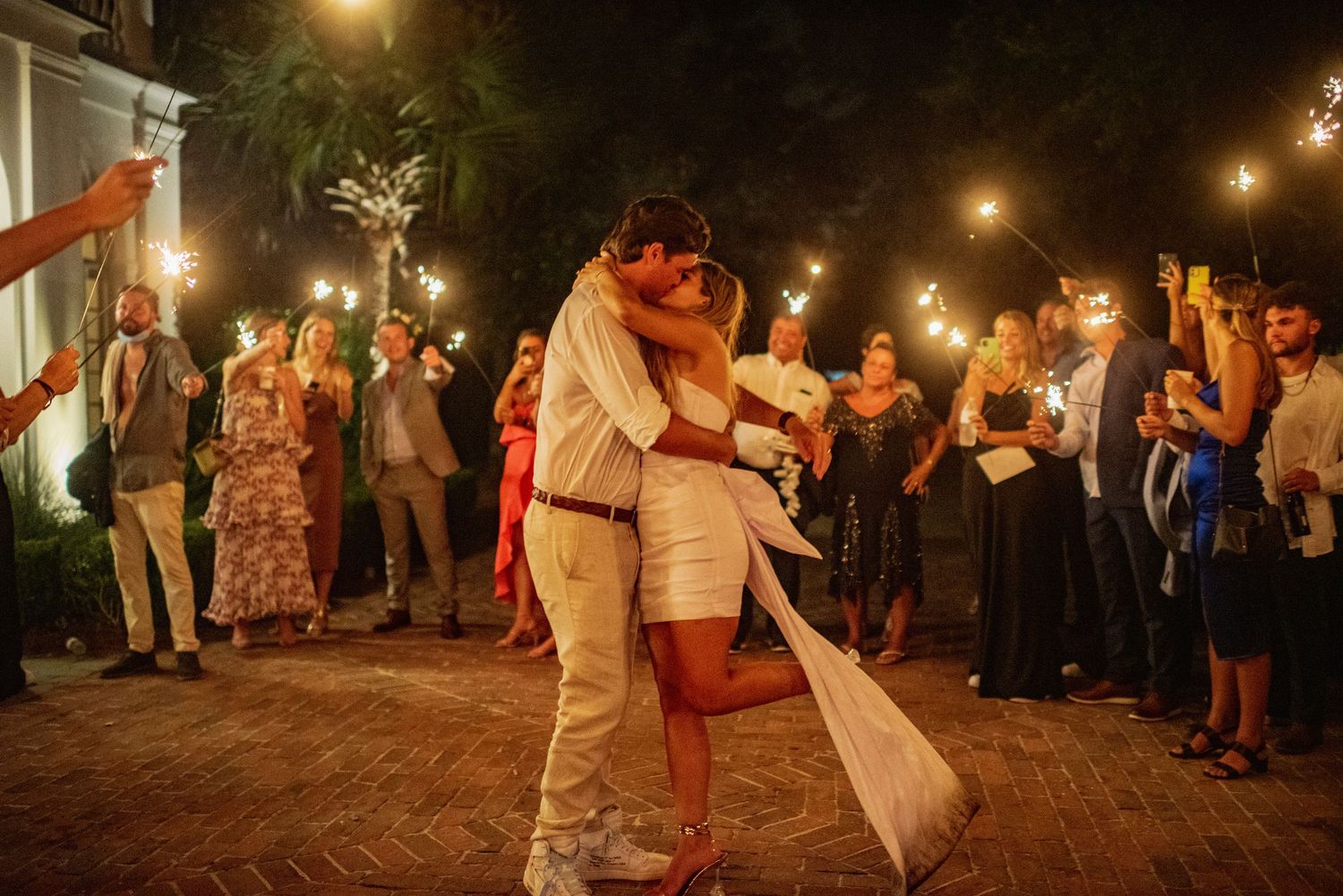 A couple shares their first dance at an evening wedding reception under string lights while guests watch and celebrate.
