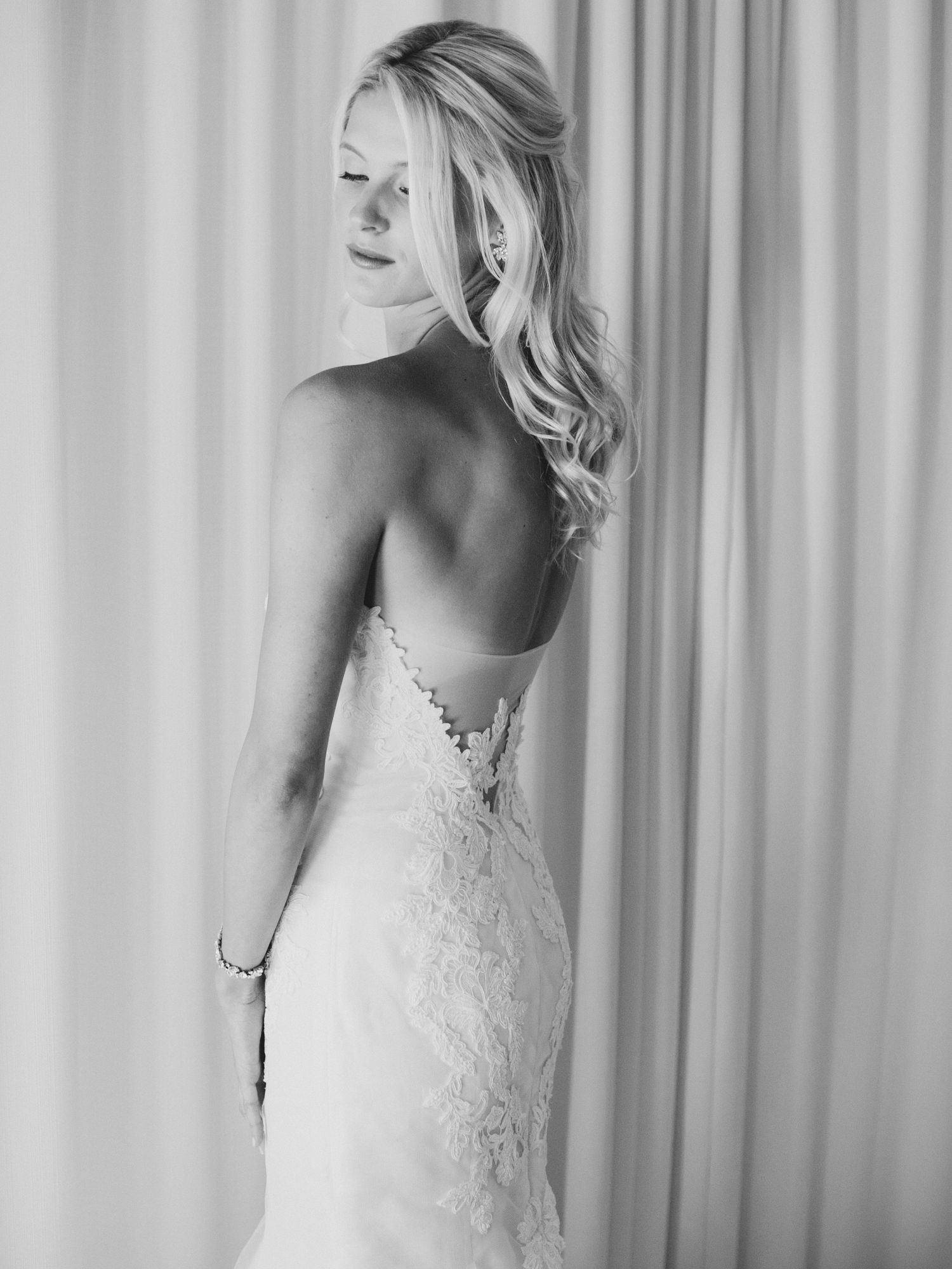 Black and white portrait showing elegant lace details of a wedding dress against a light background.