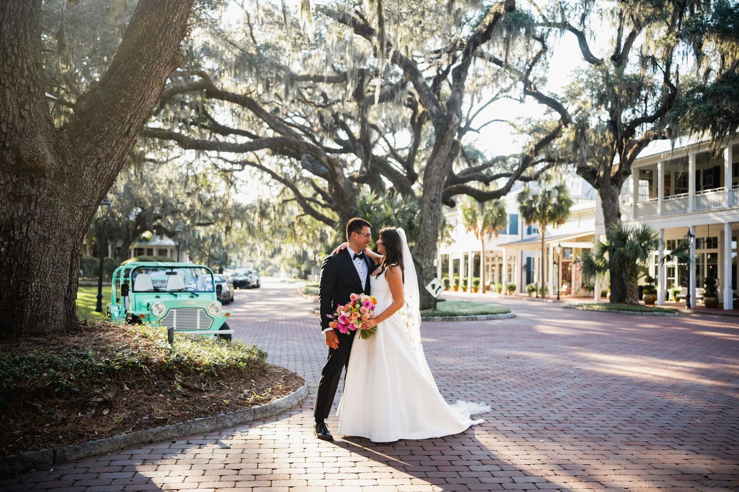 A couple shares a romantic moment on a brick-paved street lined with Spanish moss-draped oak trees and historic buildings.