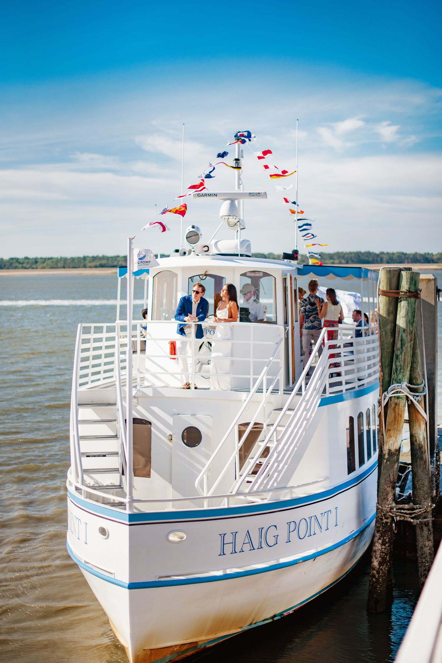 A white yacht named Haig Point docked at a waterfront pier with blue trim and multiple flags flying.