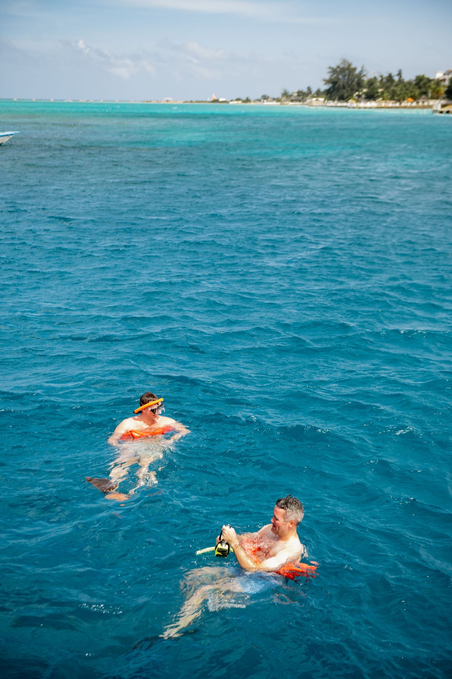 Snorkelers swim in crystal clear turquoise waters off a tropical beach coastline.