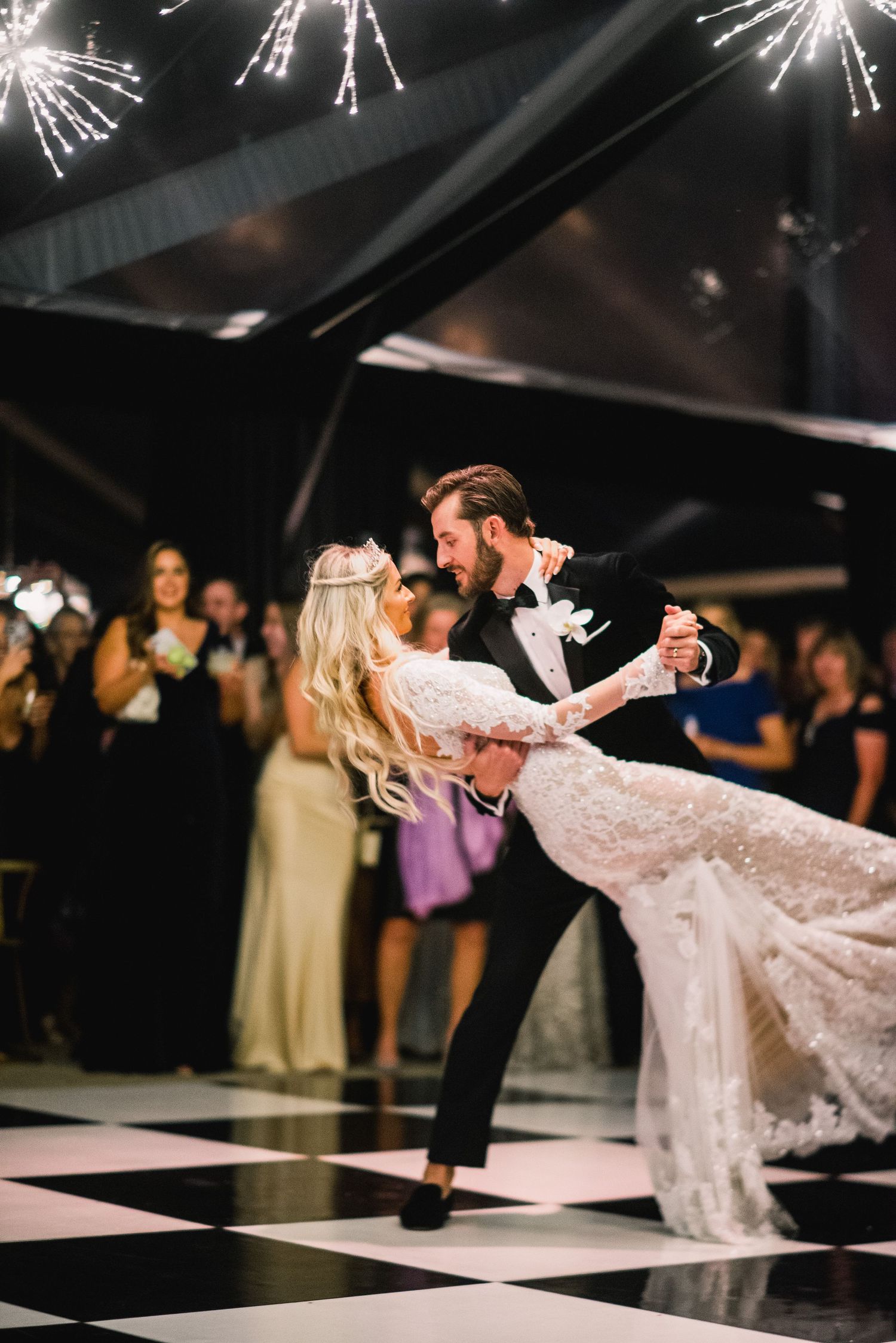 A couple performs an elegant dip dance move on a black and white checkered dance floor at a wedding reception.