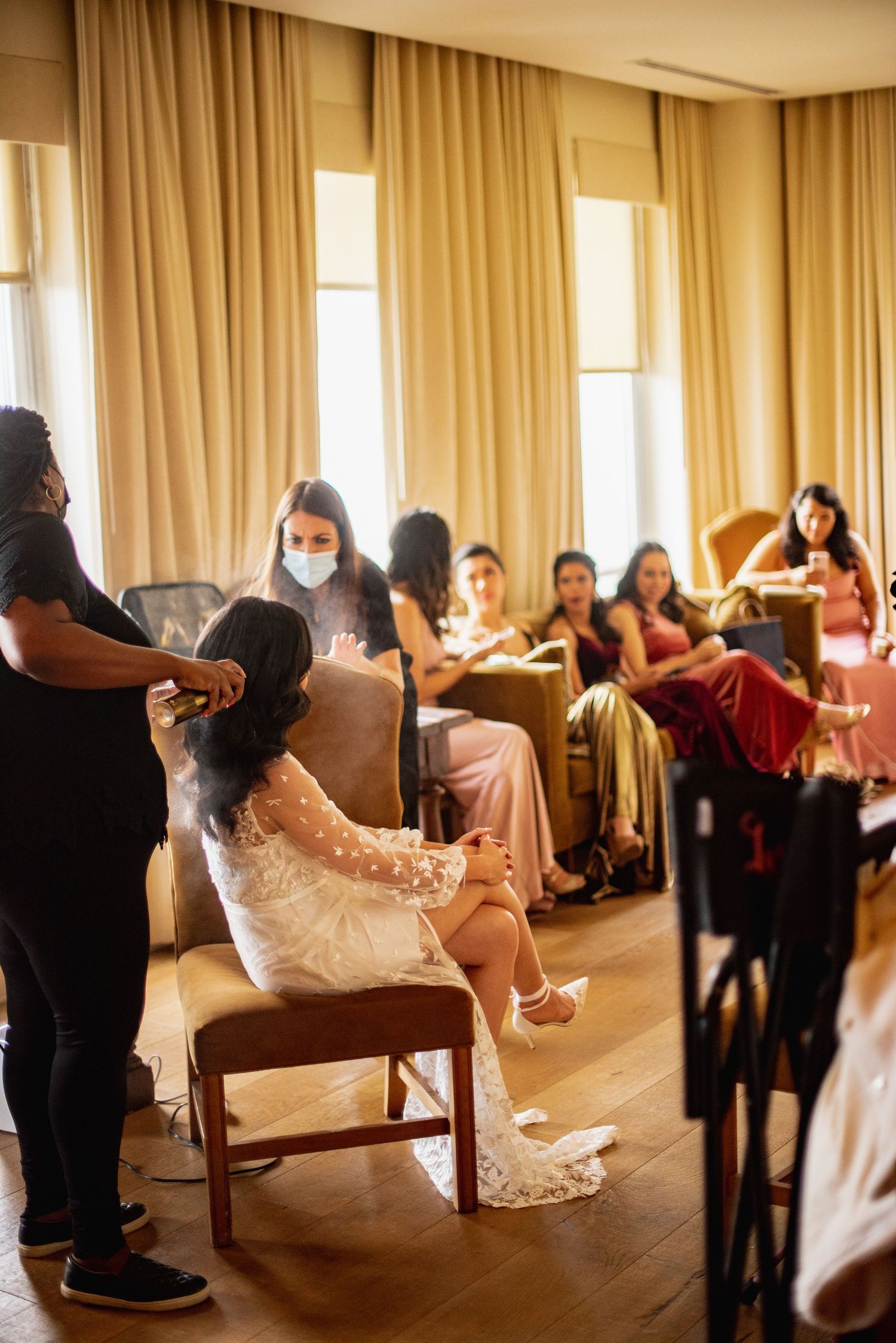 Wedding guests participate in a group dance activity in a sunlit banquet room with golden curtains.