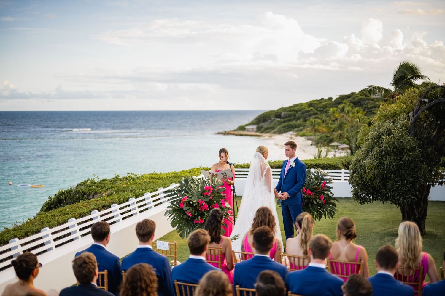Wedding guests seated outdoors overlooking a scenic ocean vista with tropical greenery.