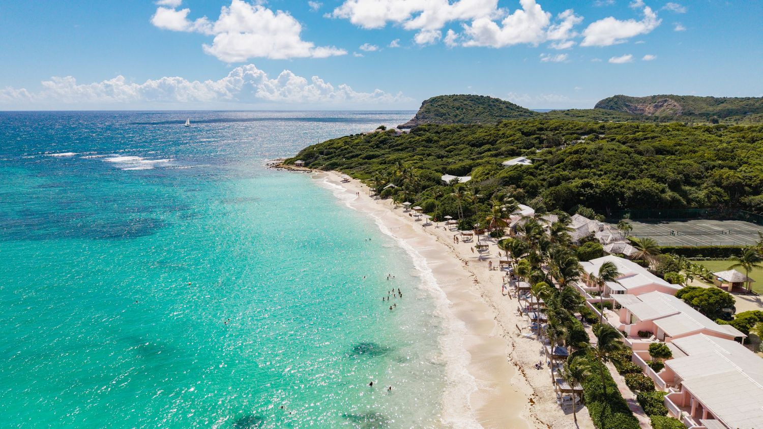 Panoramic aerial view of a pristine beach with turquoise waters and lush green coastline under blue skies.