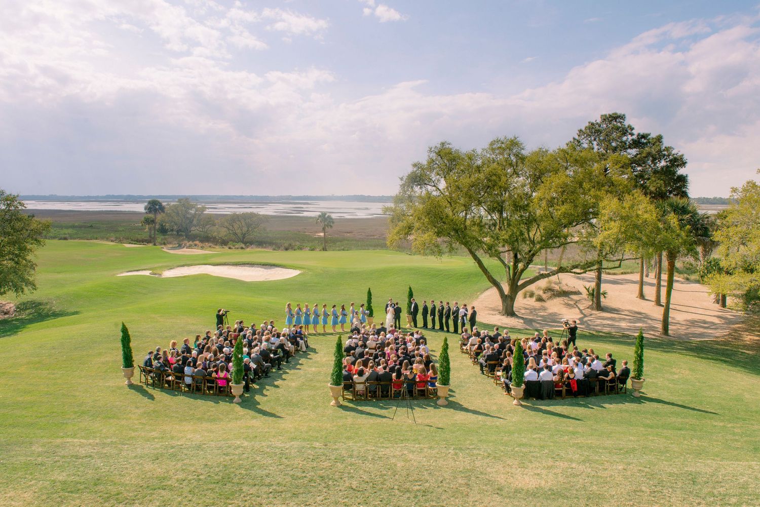 Outdoor wedding ceremony setup with guests seated in curved rows on a lush green golf course overlooking a scenic lake.