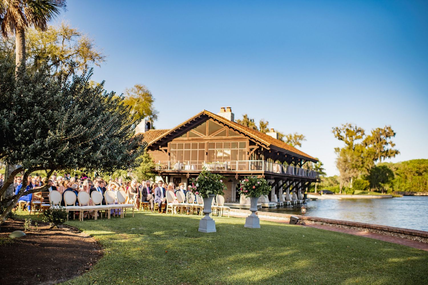 A panoramic view of a rustic lakeside venue with palm trees and wooden buildings during a sunny afternoon.