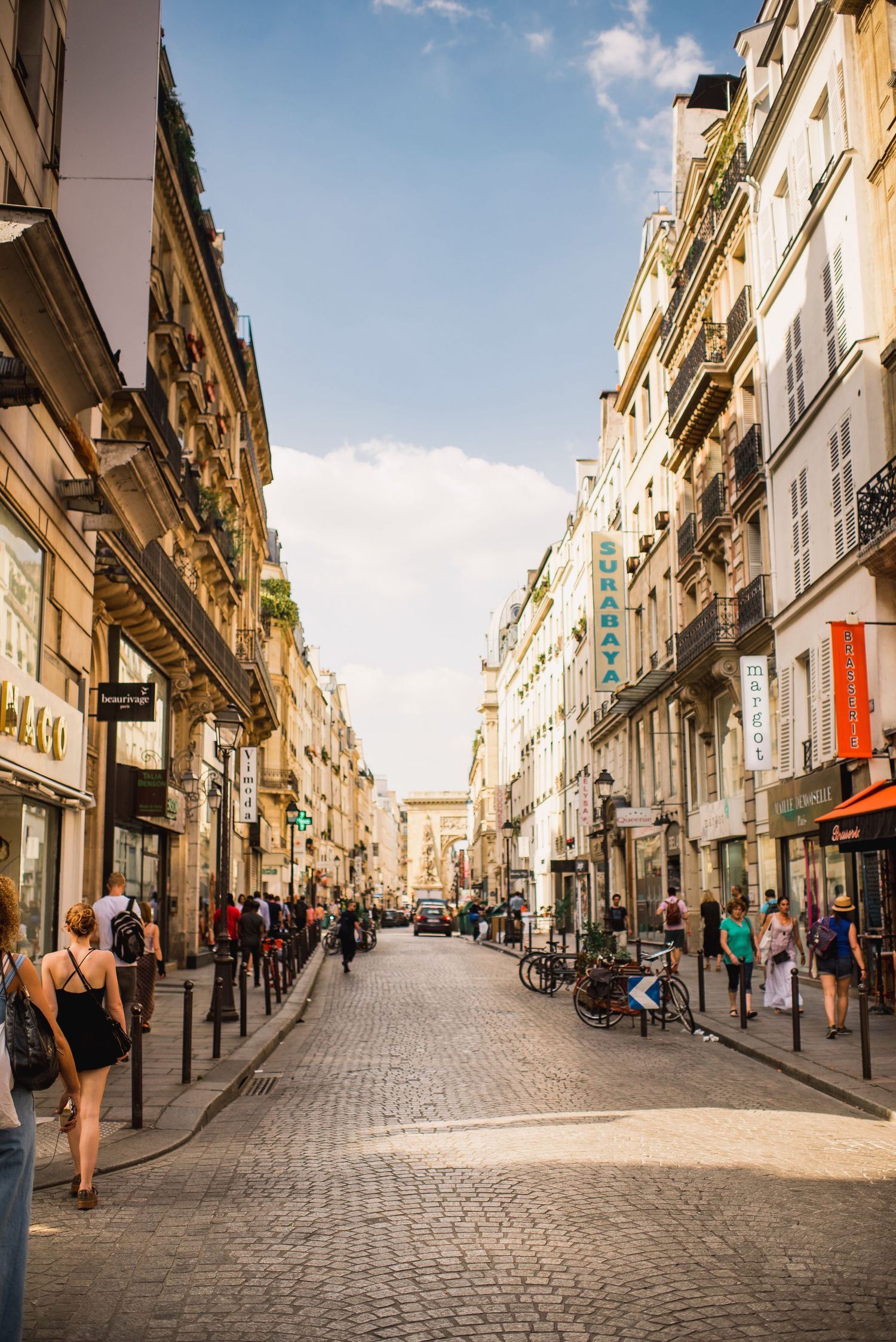 Historic European cobblestone street lined with classic architecture and shops in warm sunlight.