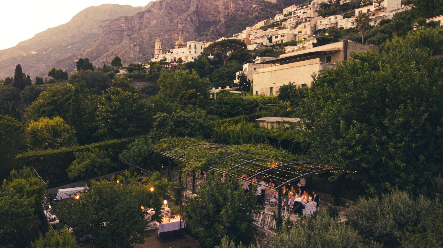 Panoramic view of a Casa Privata in Praiano, IT nestled among Mediterranean mountains at sunset.