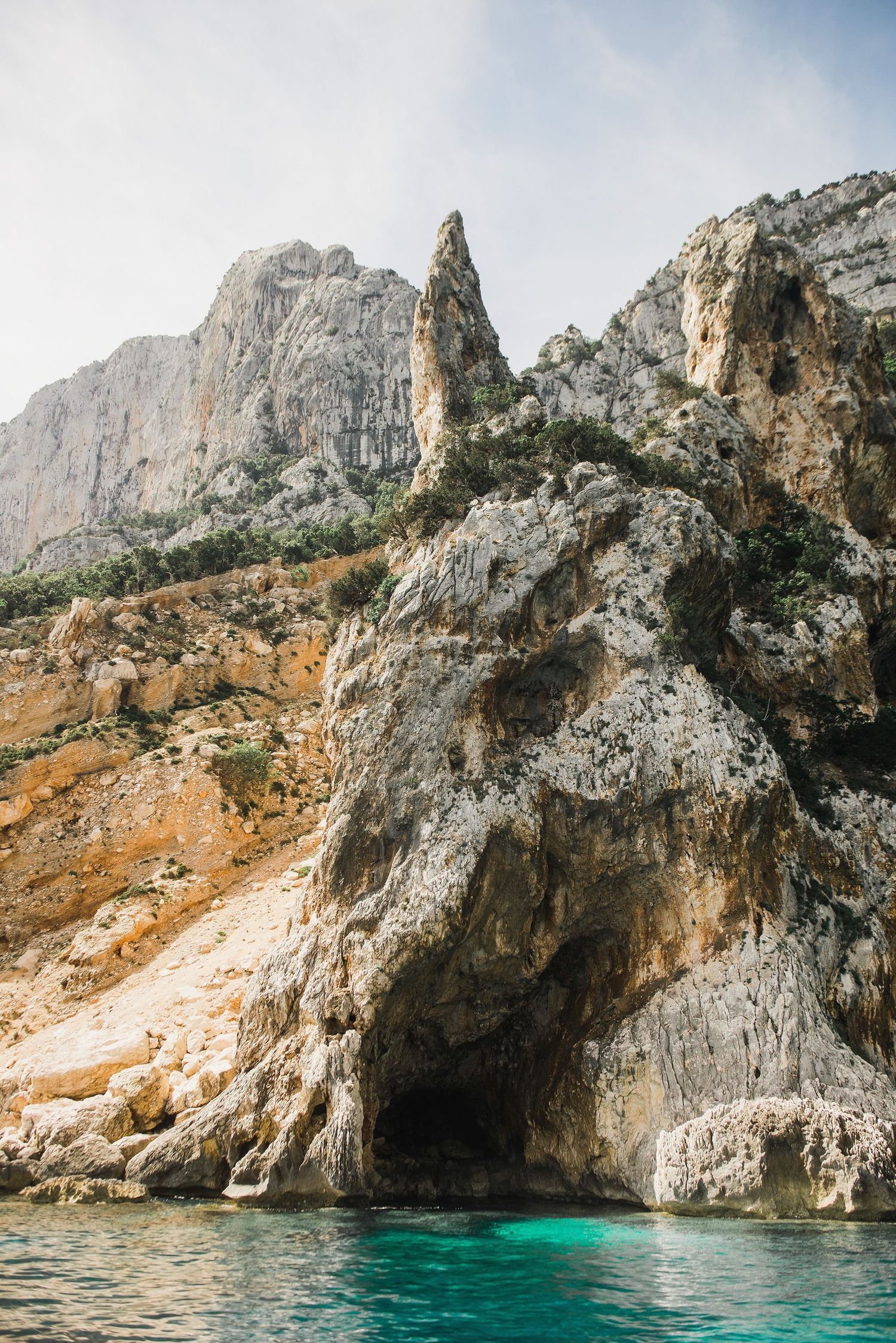 Dramatic limestone cliffs rise from crystal clear turquoise Mediterranean waters along a rocky coastline.