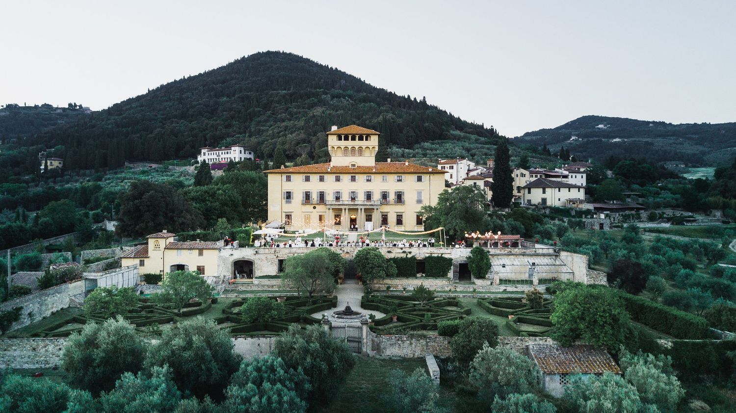 Panoramic view of a Mediterranean hillside village with white buildings and green mountains in the background.