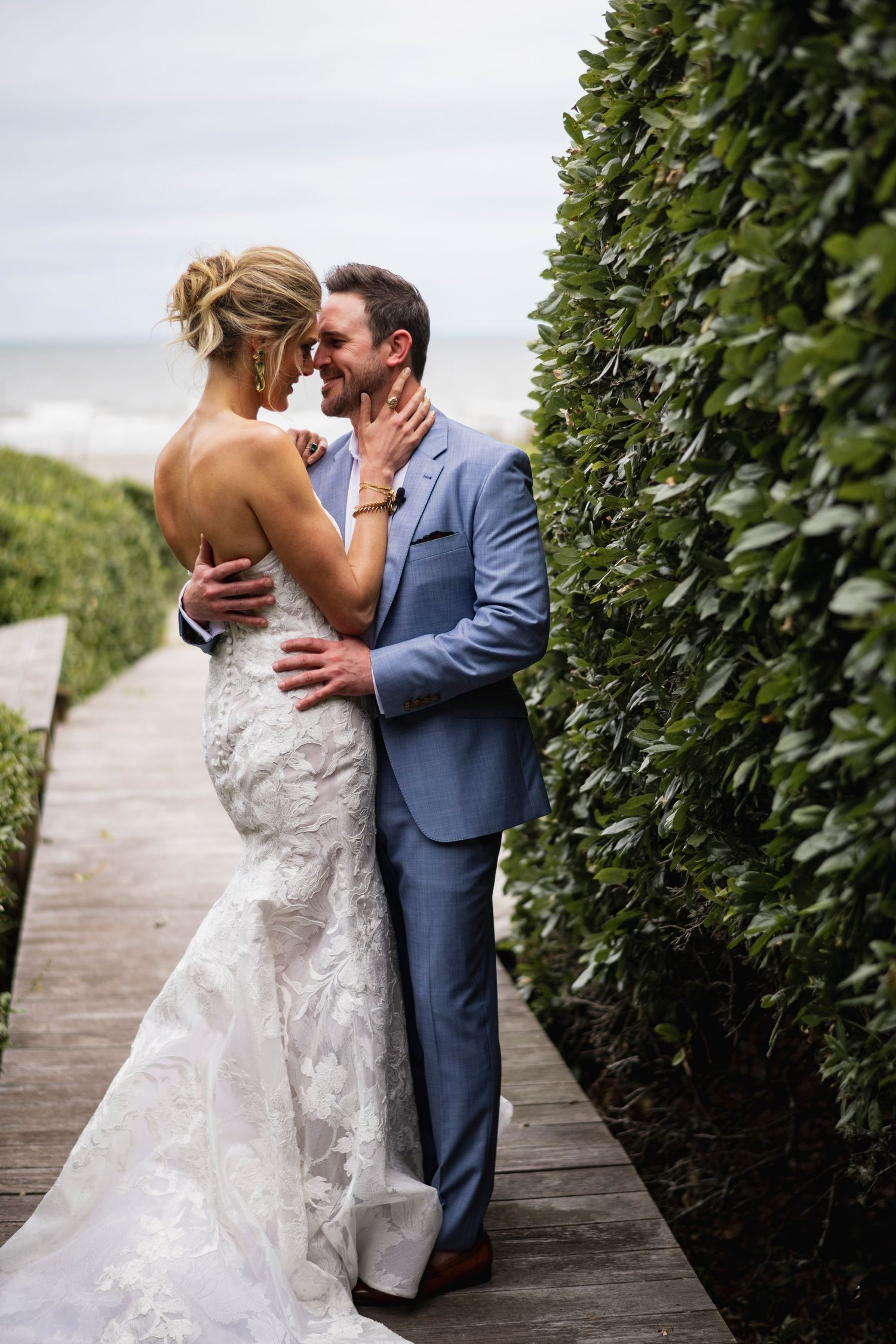 A romantic wedding couple shares passionate kisses on a wooden boardwalk surrounded by lush green foliage.