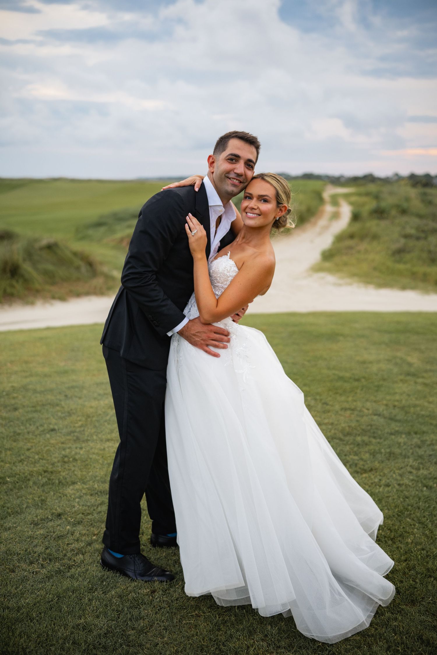 Wedding couple embracing on a grassy hilltop with scenic coastal views.