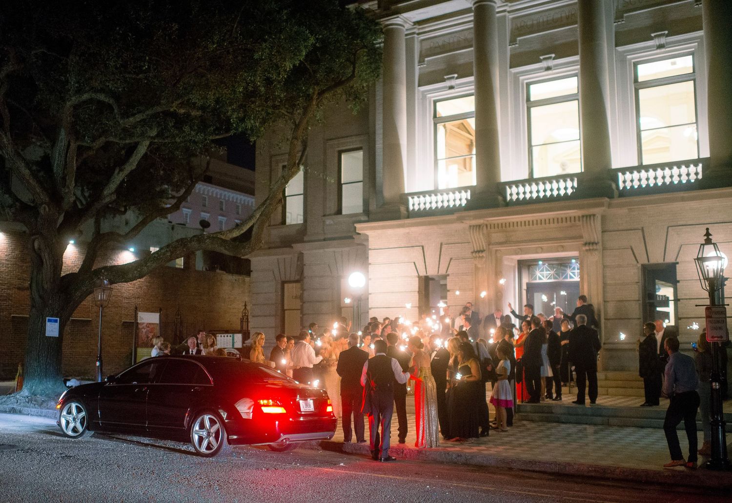 People gather outside a building at night with car headlights illuminating the scene.