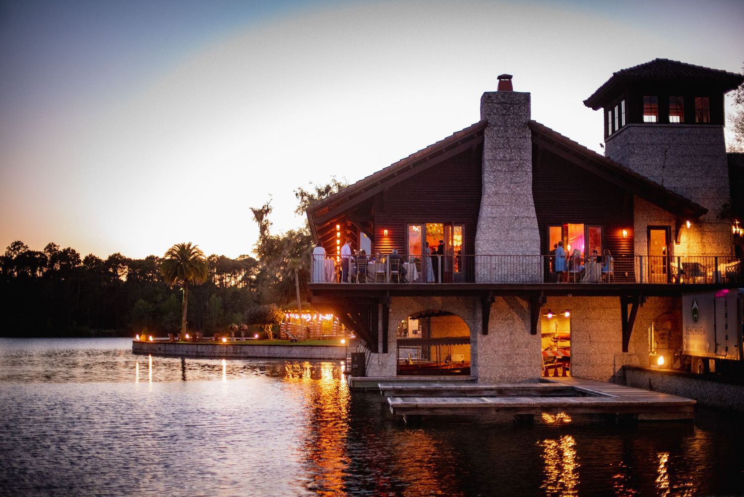 Lakeside gazebo and dock illuminated at sunset with warm glowing lights reflecting on calm waters.