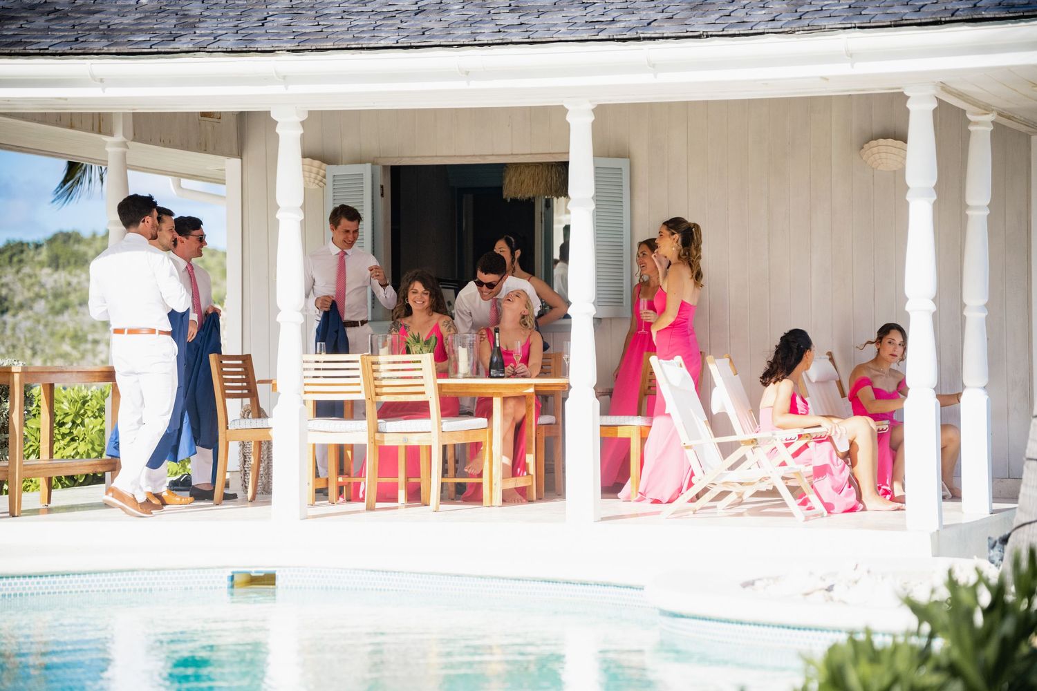 Group gathered on white veranda deck next to swimming pool at tropical resort.