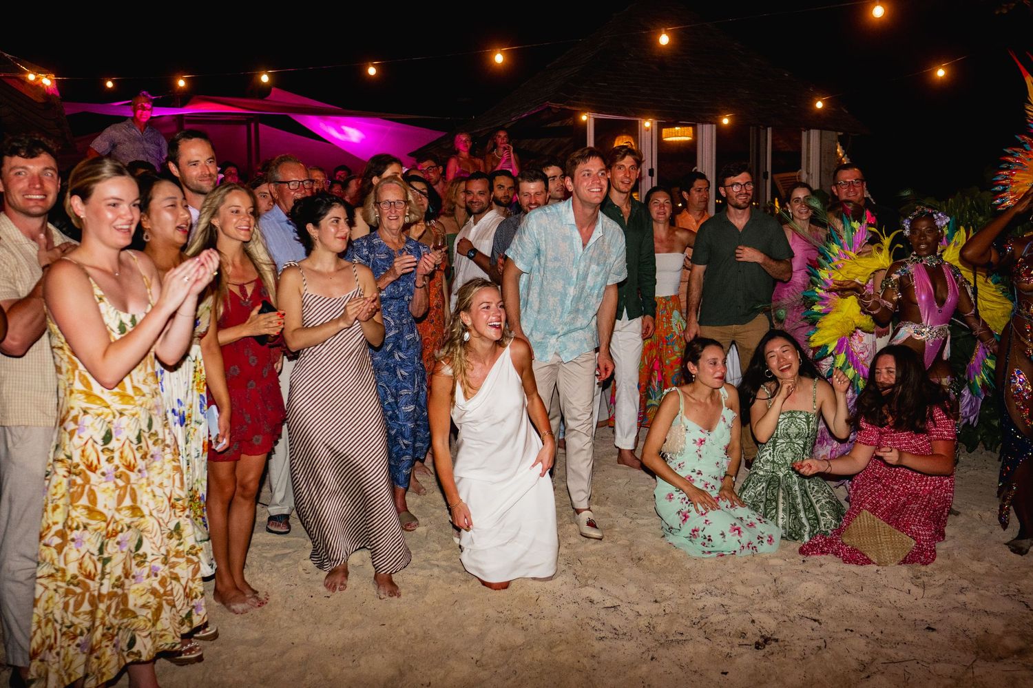 Large group celebrating at a beachside party with colorful lighting and festive atmosphere.