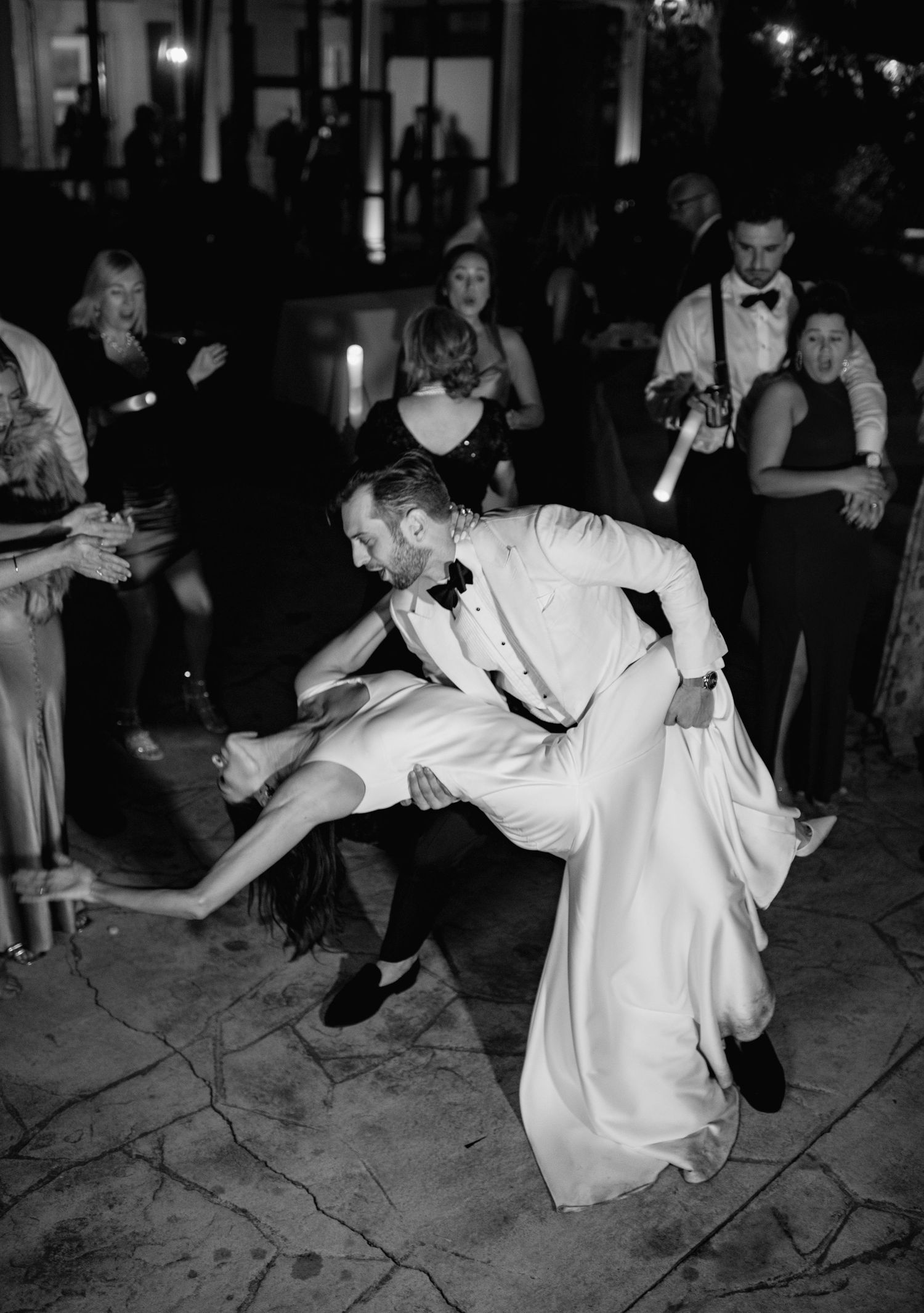 A couple dances together at a wedding reception, performing an energetic dip move on the dance floor.