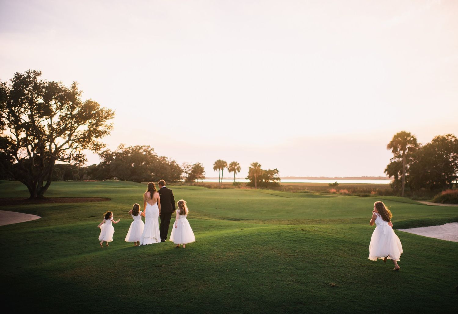 Silhouettes of people walking on a grassy hill at sunset with golden light illuminating the landscape.