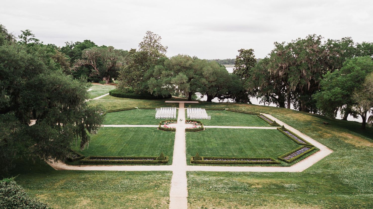 Aerial view of a symmetrical garden with manicured lawns and pathways forming geometric patterns surrounded by trees.
