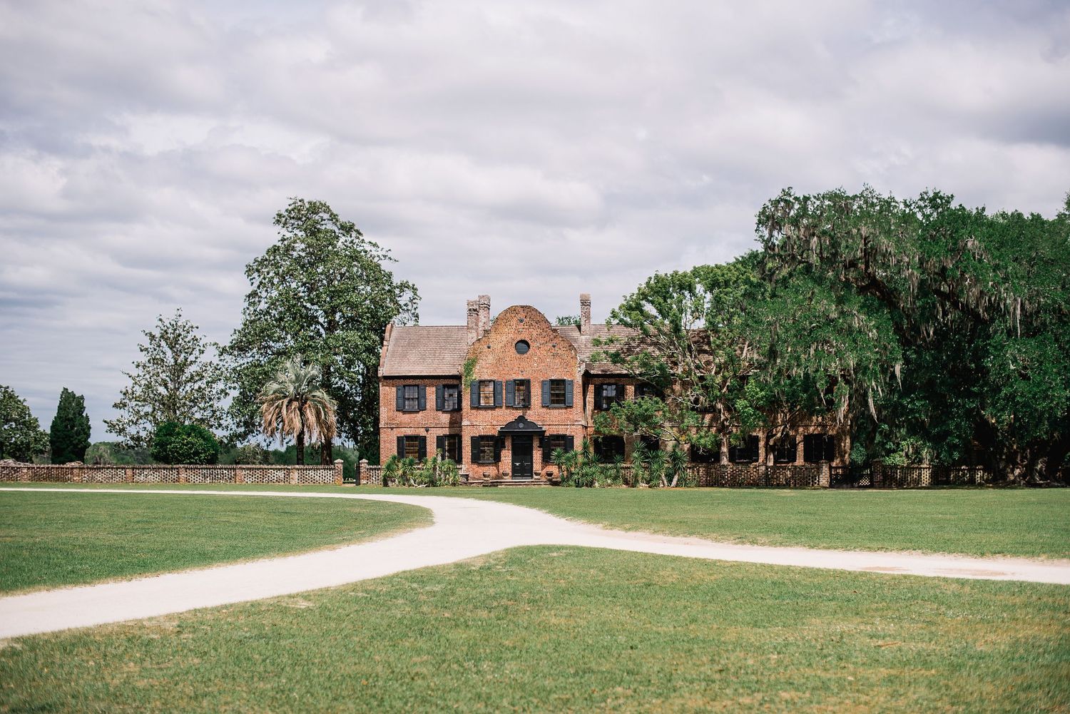 A scenic winding driveway leads through green landscaping to a grand Spanish-style estate mansion.