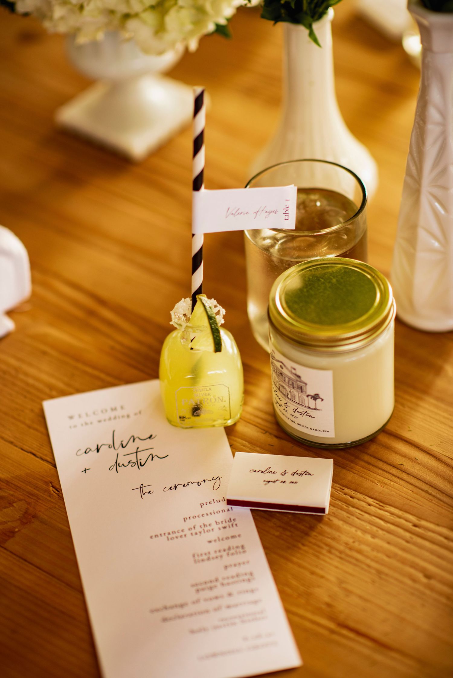 Wedding menu cards and cocktail glasses with green drinks and straws sit on a wooden table in warm lighting.