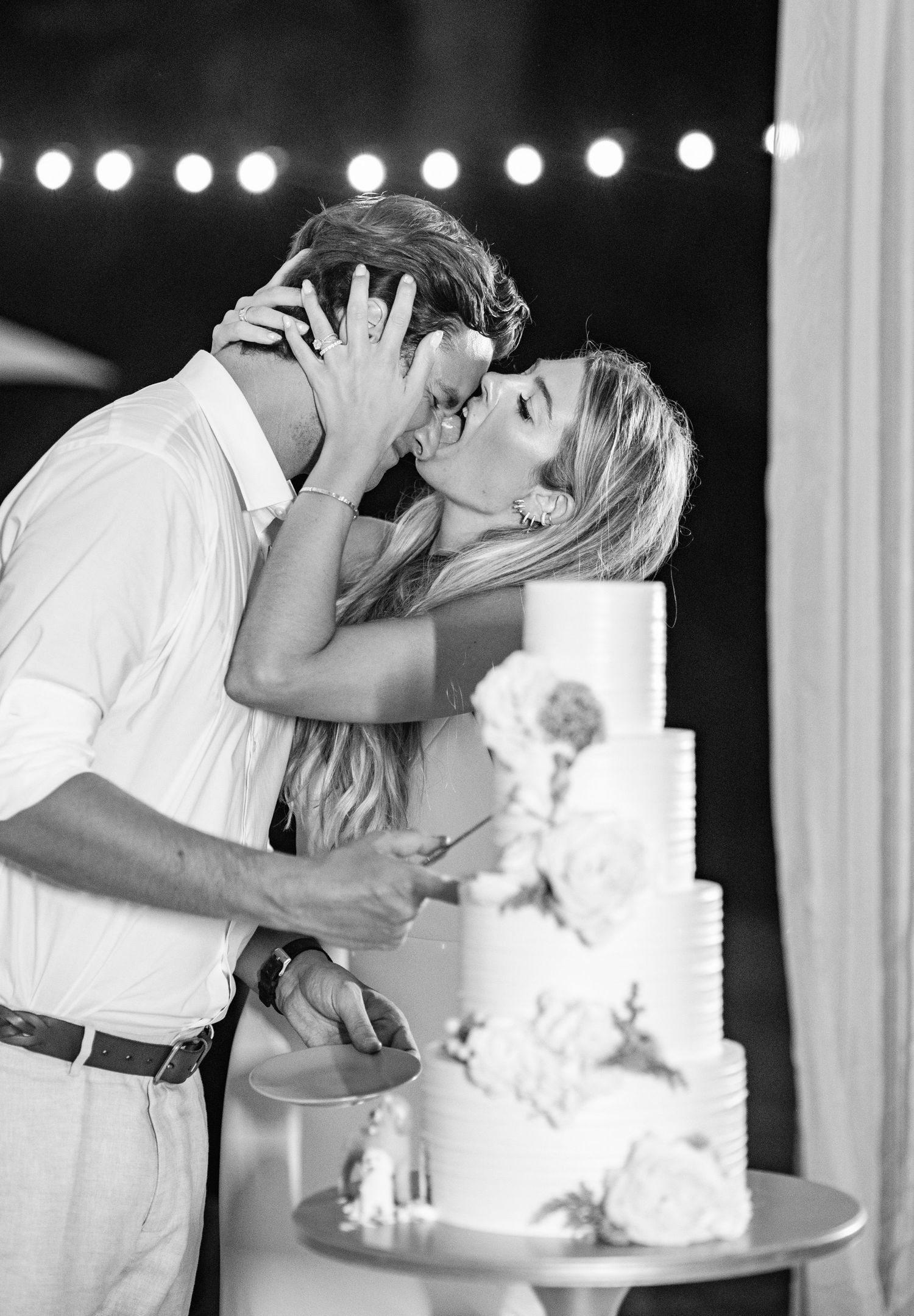 A romantic black and white wedding photo series showing a couple kissing next to their elegant white wedding cake.