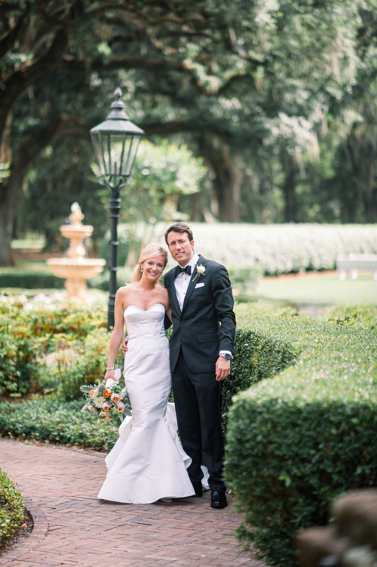 A bride and groom share joyful moments together in a lush garden setting with brick pathways and ornamental decor.