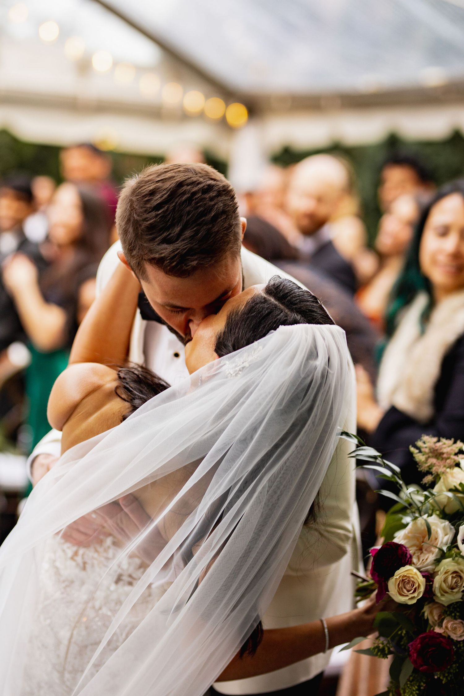 A romantic wedding moment captured as a couple shares a kiss under a flowing white veil at their reception ceremony.