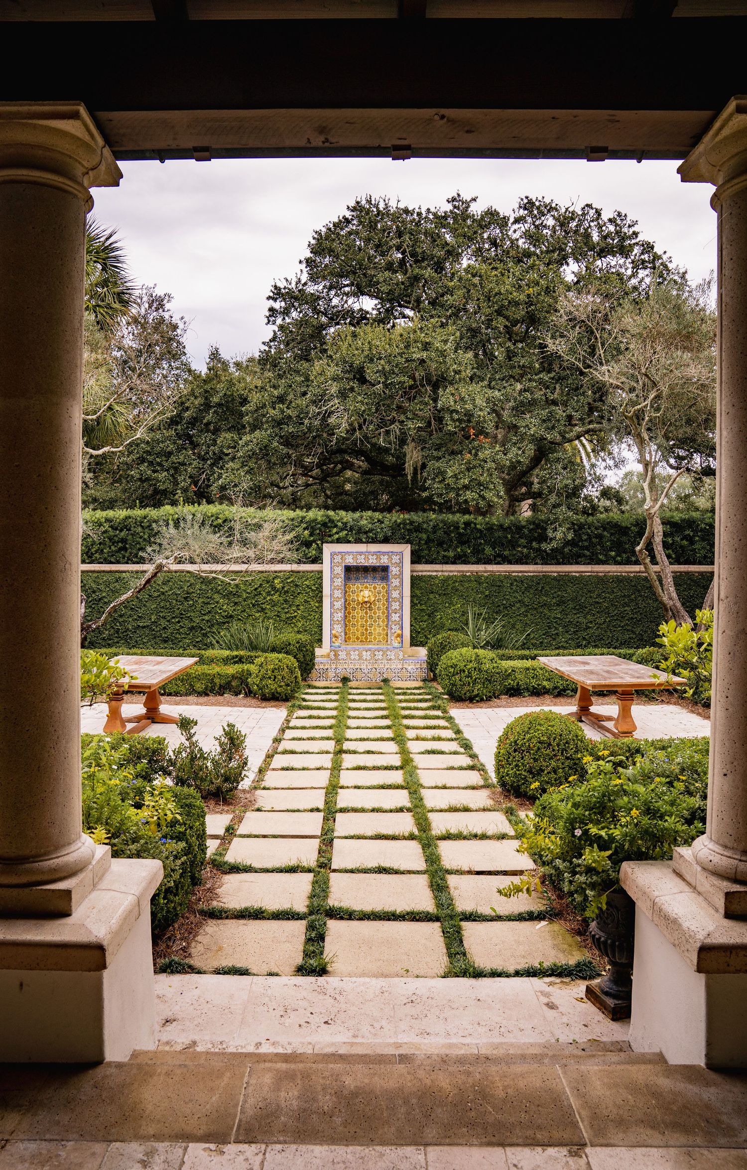A formal garden terrace with stone pavers, columns, and manicured hedges creates a symmetrical outdoor space.