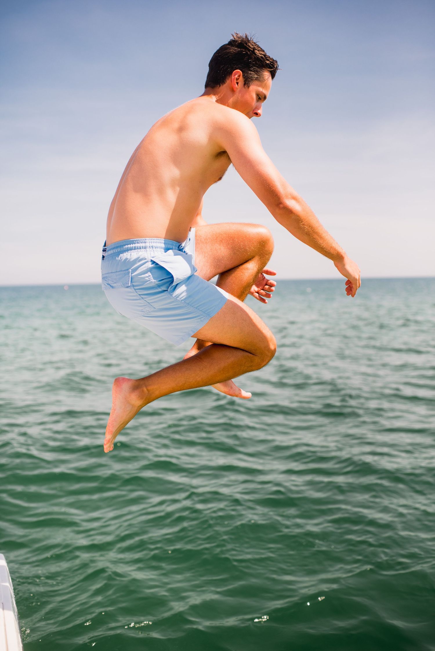 Person in blue swim shorts jumping into turquoise ocean water on a sunny day.