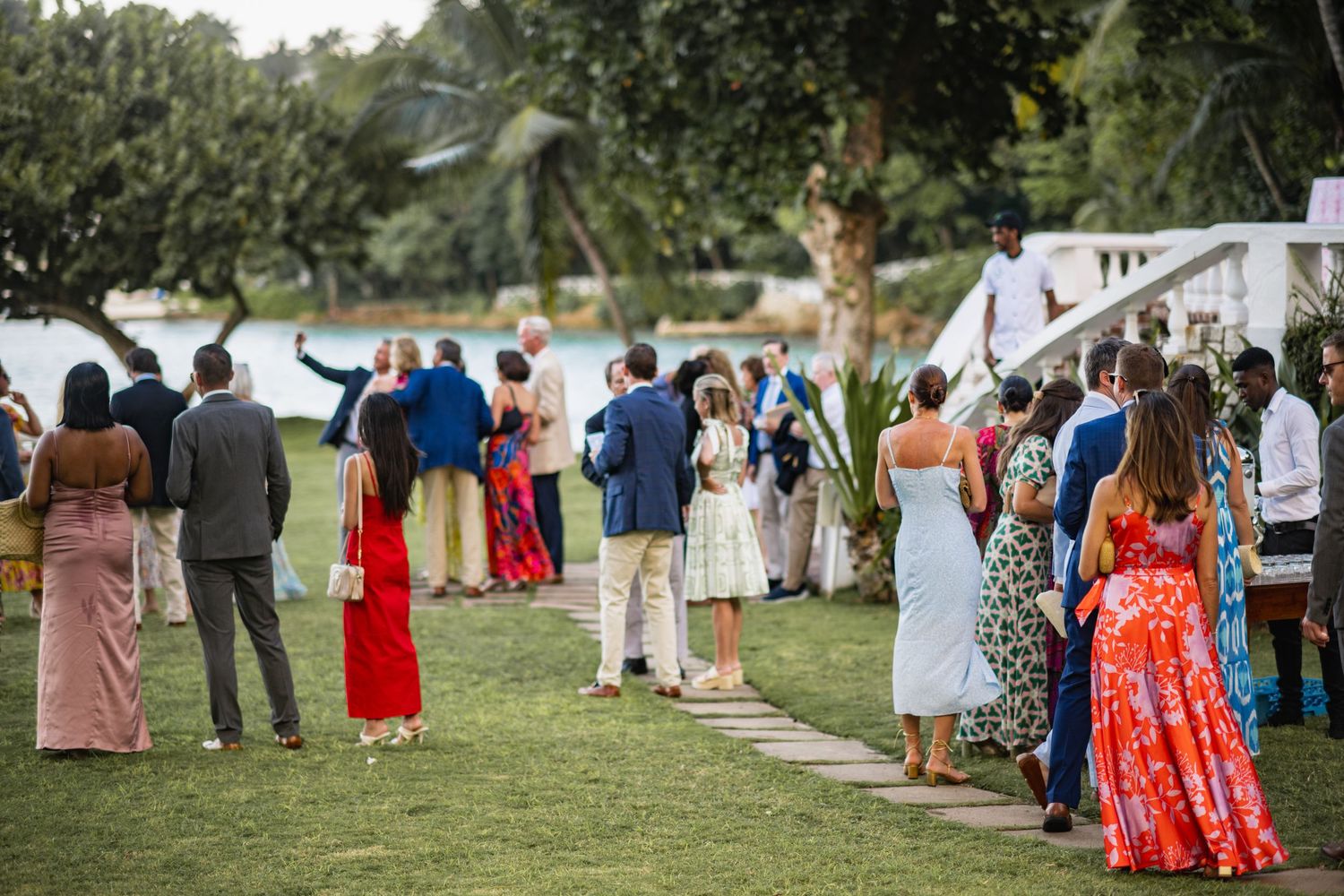 Guests in colorful formal attire mingle on a lush green lawn at an outdoor garden party reception.