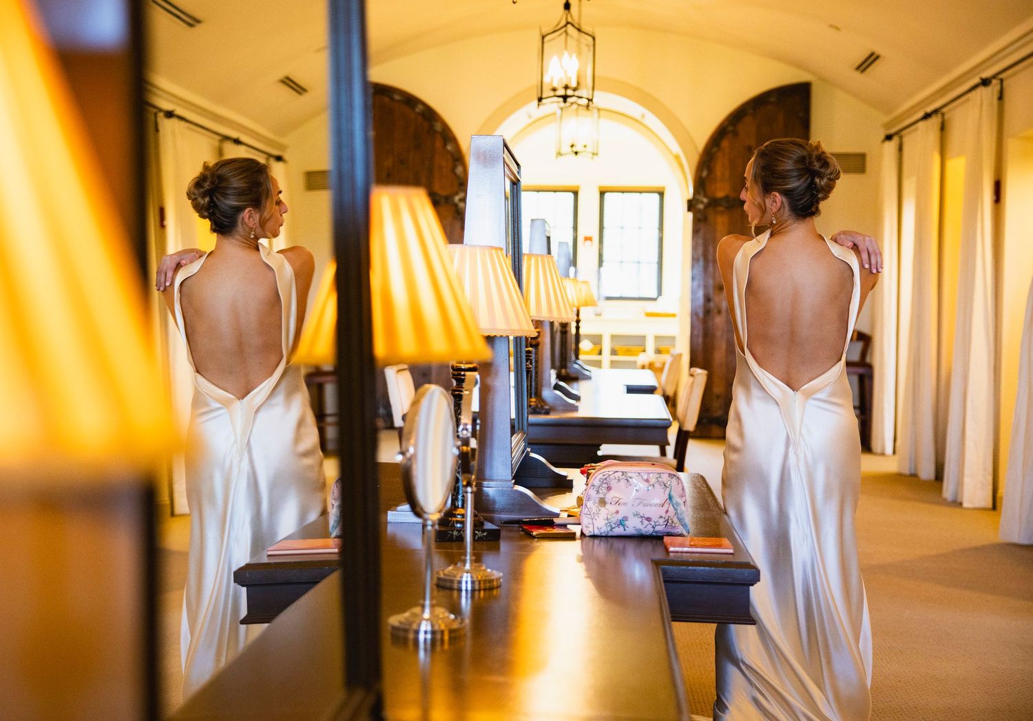 A person in a white dress walks through an elegant hallway with warm lighting and arched doorways.