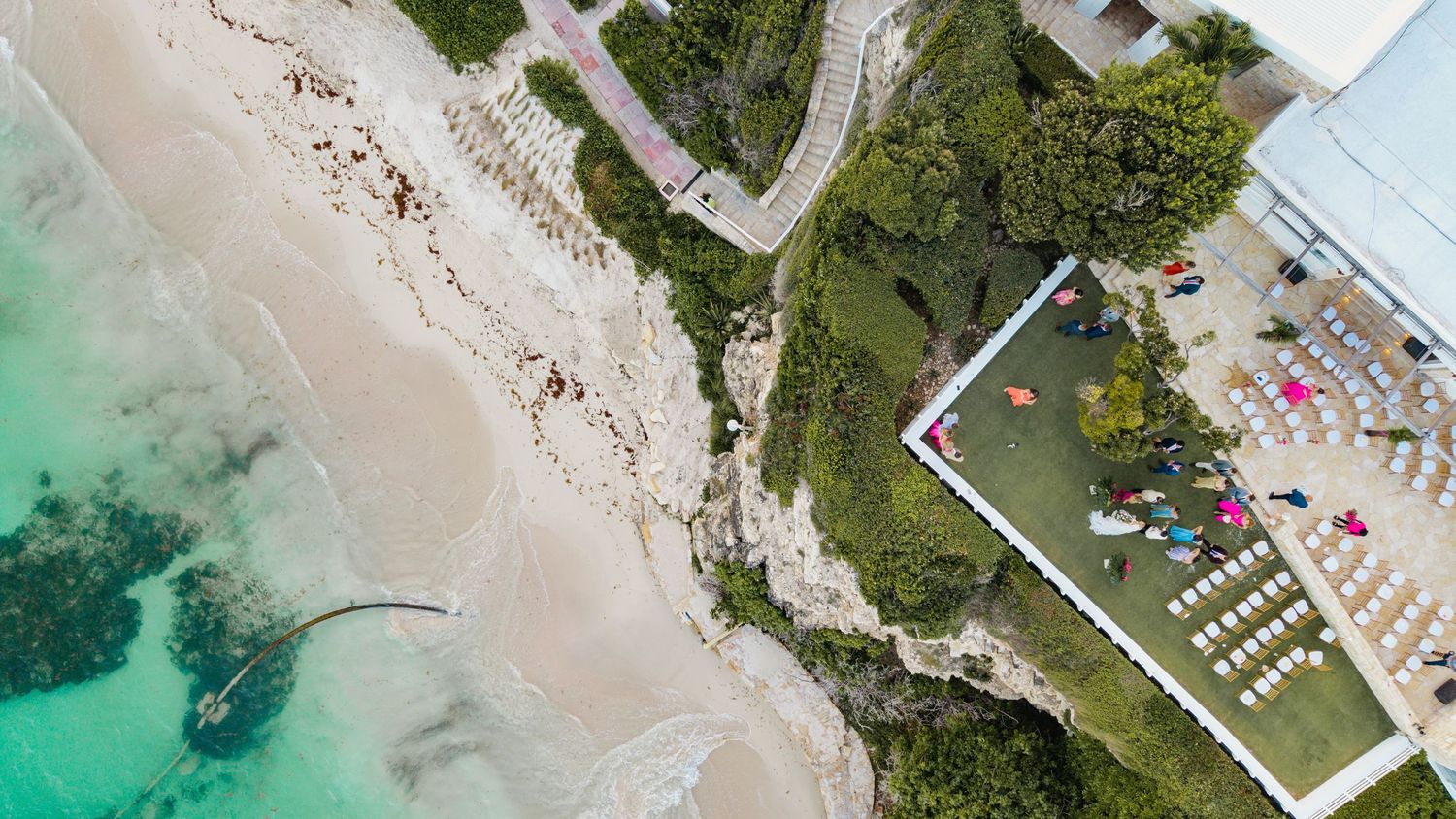 Aerial view of a pristine white sandy beach with turquoise waters and green coastal vegetation along the shoreline.
