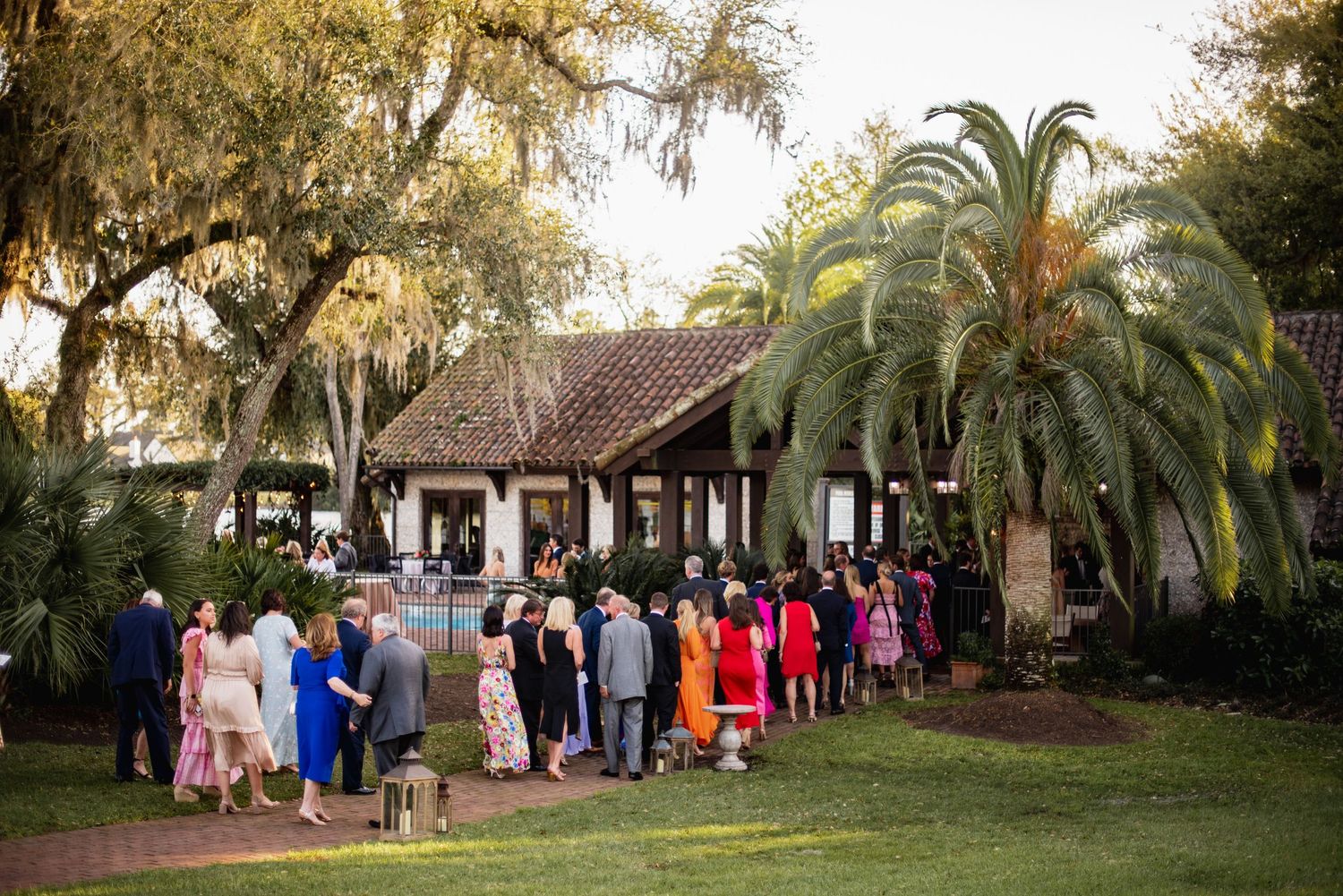 Wedding guests gather in a lush garden setting with palm trees and tropical landscaping during an outdoor celebration.