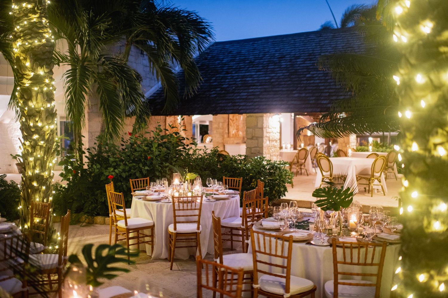 Elegant outdoor wedding reception setup with string lights and tropical garden decor.